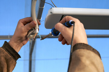 Ceiling-mounted infrared heater in the greenhouse. Wiring of the electric cable in the protective tube. Tinning of wire contacts. Men's hands with a soldering iron.