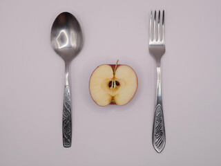 On a light background, a spoon, a fork and half an apple, top view