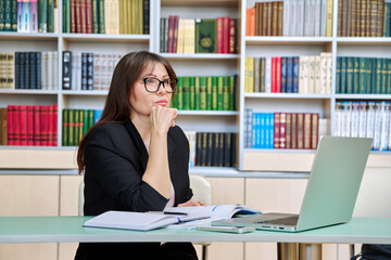 Middle aged female teacher working inside library office with laptop