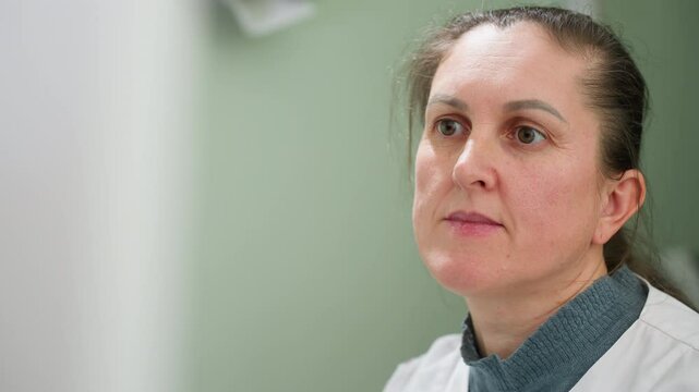 Matron in lab coat attentively making medical observations during diagnostic procedure with focused expression in clinical setting under bright lighting, showcasing concentration and professionalism