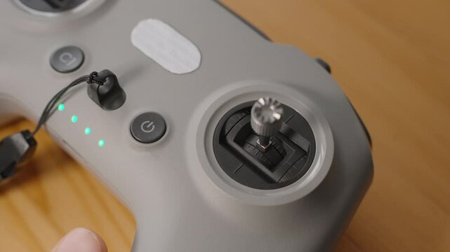 Finger Pressing Power Button on FPV Drone Controller with Connected Joystick and Active LED Indicators, Close-Up Macro View, Startup Concept