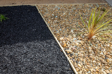 A landscape design showcasing a clean division between black wooden mulch and pale pebbles, with a linear edge separating two complementary weed-control materials in a modern garden landscaping.