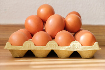 Fresh brown eggs stacked in a carton on wooden kitchen counter ready for cooking or baking