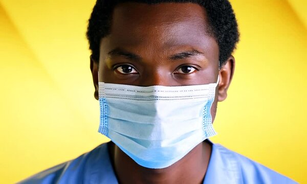 A young Asian guy displays a serious expression, wearing a surgical mask against a vibrant yellow backdrop, symbolizing health and safety in contemporary settings.
