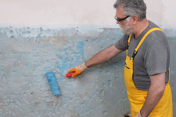 Worker using paint roller to apply adhesive primer fluid for gluing tiles