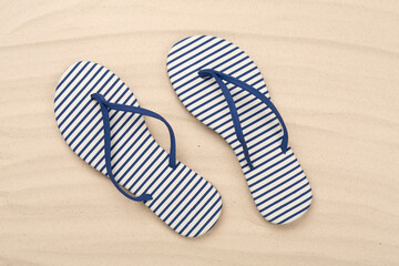 Striped blue flip-flops on sand background, top view