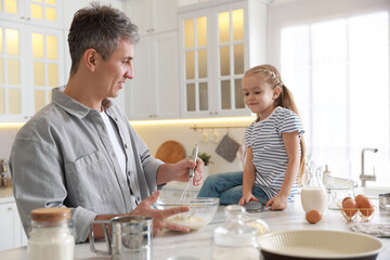 Father and his daughter making dough at white marble table in kitchen