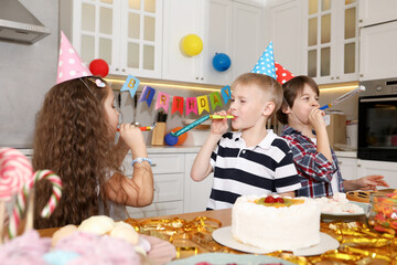 Children in conical paper hats with blowers celebrating birthday indoors. Surprise party