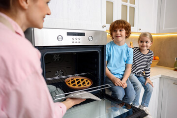 Mother and her kids taking out pie from oven in kitchen, closeup