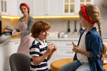 Happy kids eating tasty cookies while their mother baking in kitchen, selective focus
