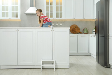 Little girl sitting on counter near step stool in kitchen