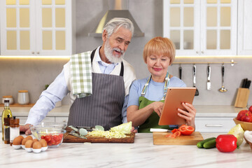 Senior couple using tablet while cooking together in kitchen