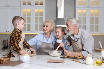 Grandparents and their grandkids cooking together at white marble table in kitchen