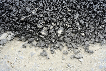 Freshly dumped asphalt on road surface
Black asphalt material spread over a pale roadbed, showing a clear contrast between the rough pavement mix and the base layer.

