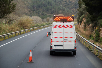 Road maintenance van with a warning light panel for roadworks, on a newly paved road, rear view.