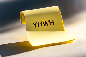 A yellow scroll with the sacred name "YHWH" is illuminated by gentle sunlight on a smooth surface.