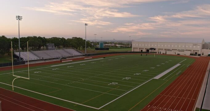 Wide aerial shot of an empty high school American football field at sunrise.