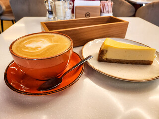 Coffee and cheesecake, orange cup of coffee and a slice of cheesecake on a table in a cafe