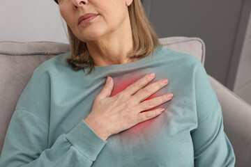 Heart attack. Senior woman suffering from pain in chest on sofa at home, closeup