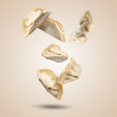 Uncooked gyoza falling on dark beige background