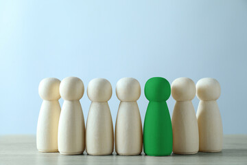 Difference, uniqueness, individuality. Green human figure among wooden ones on light background