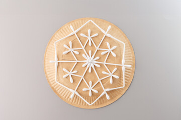 Creative craft project with a paper plate and cotton swabs forming a symmetrical snowflake or star. Perfect for school activities, craft blogs, instructional guides, DIY brands, art supply promotions.