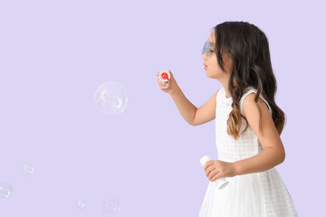 Cute little girl blowing soap bubbles on lilac background