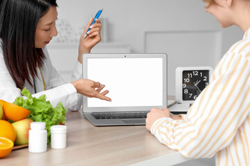 Female Asian nutritionist with laptop and patient in office