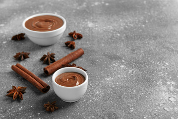 Bowls of tasty melted chocolate with cinnamon sticks and star anise on grey grunge background