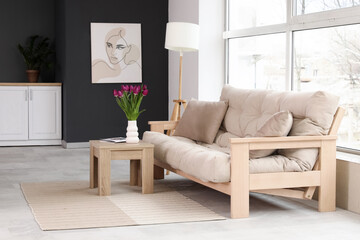 Stylish interior of black-and-white living room with cozy sofa, lamp and tulips on coffee table
