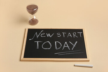 Blackboard with text NEW START TODAY and hourglass on beige background