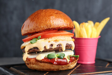 Wooden board with tasty burger and french fries on black grunge background, closeup