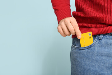 Young man putting credit card in jeans pocket on blue background, closeup