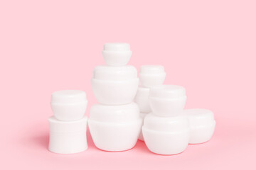 Set of jars with cosmetic products on pink background