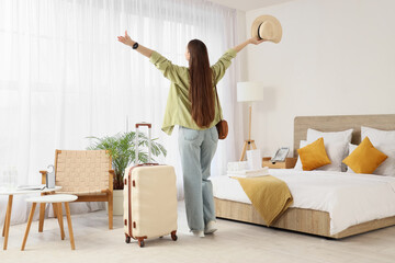 Happy female tourist with suitcase in hotel room