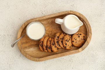 Wooden tray of sweet cookies with chocolate chips and glass of milk on white background