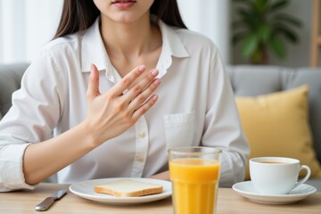 A young adult Asian woman in a white shirt enjoys breakfast at home with toast, orange juice, and coffee, featuring a cozy and inviting atmosphere in a modern living space.