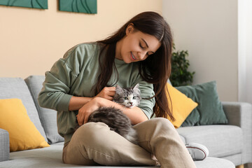 Obraz premium Young woman pet her cute longhaired cat and sitting on sofa in living room