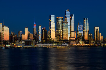 Naklejka premium A breathtaking view of Midtown Manhattan at night, featuring the Empire State Building glowing among a forest of illuminated skyscrapers