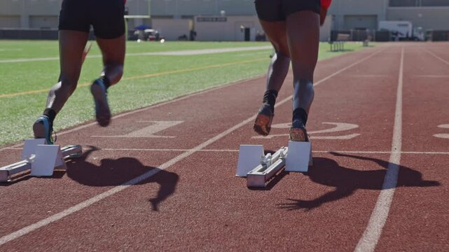 Two high school runners sprint off of starting block on a practice track