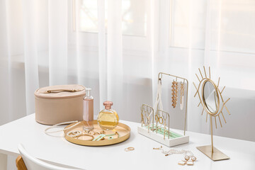 Organizers with stylish different jewelry, mirror and perfume bottles on table near window