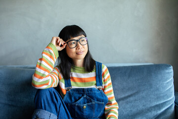 Asian woman in striped sweater and overalls sitting on blue couch