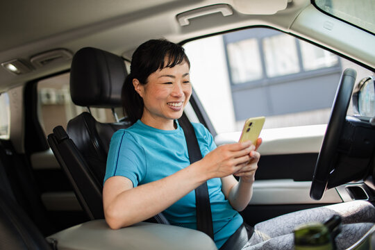 Smiling Asian woman texting on smartphone wearing sport clothes inside a car
