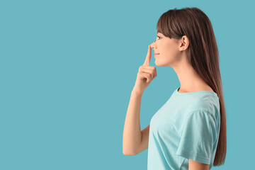 Beautiful young happy woman touching her nose on blue background. Plastic surgery concept