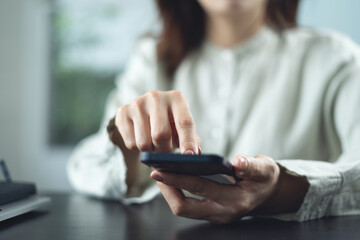 Close up, business woman using mobile phone during working in office, finger touching on phone screen. Woman using smartphone searching the information, surfing the internet at workplace