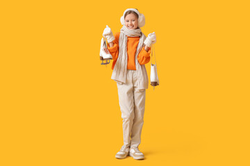Beautiful young girl in winter clothes holding ice skates on yellow background