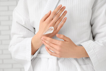 Fototapeta premium Young woman applying cosmetic cream on her hands against white brick background, closeup