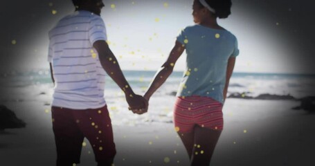Couple holding hands walking on beach with golden sparkles animation overlay - Powered by Adobe