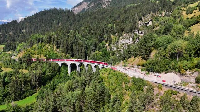 Train driving in Scenic Swiss Apls landscape passing over the iconic Landwasser Viaduct before disappearing into a tunnel