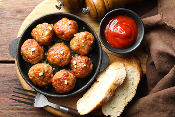 Tasty meatballs with green onion in baking dish served on wooden table, flat lay
